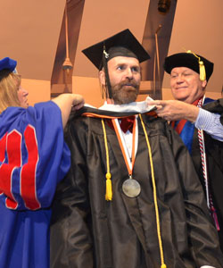 Michael Fletcher Tester, seen here receiving his academic hood for completing his master's, was a student speaker for the 2015 commencement ceremony held on Long Island.