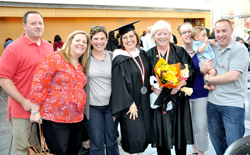 Grandmother and graduate Patricia Rampolla ’13, center right with flowers, is joined by David Rampolla, far right, Allison and Amy Rampolla, commencement speaker Carol Evans ’77, Jen and Mark Rampolla, who is holding grandson John.