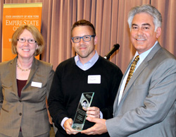 Chris Fowler, center, founder and executive director of SyracuseFirst, is presented with the college's 2014 Excellence in Environmental Sustainability Award by Nikki Shripmton, dean of the college's Central New York Center, and the 2011 award recipient Al Stirpe, (D-Cicero) who represents the people of assembly district 127.